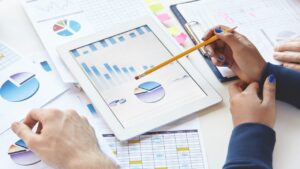 businesspeople sitting at table with touch pad and notes, developing business strategy, making changes in financial report. african girl showing presentation on tablet, pointing pencil at screen