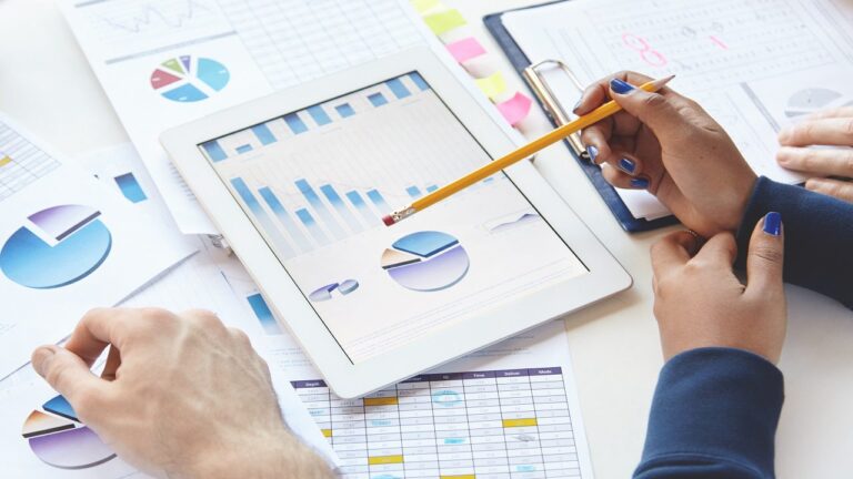 businesspeople sitting at table with touch pad and notes, developing business strategy, making changes in financial report. african girl showing presentation on tablet, pointing pencil at screen